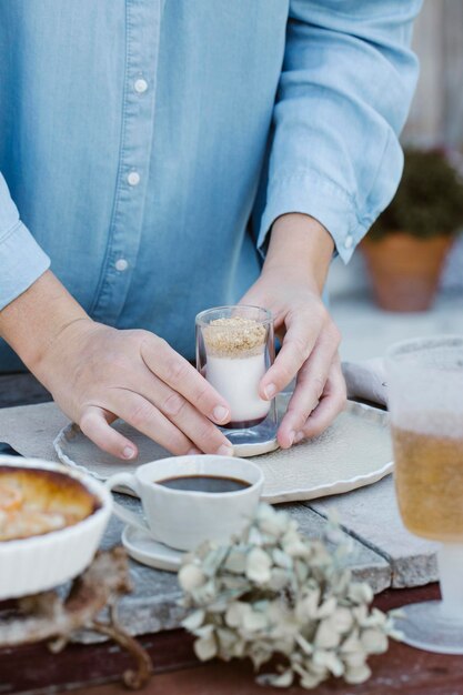 Italy, woman arranging glass of dessert on breakfast table, partial view