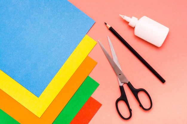 Фото Предметы для творчества листы из цветного картона, ножницы, карандаш и клей на красном вид сверху