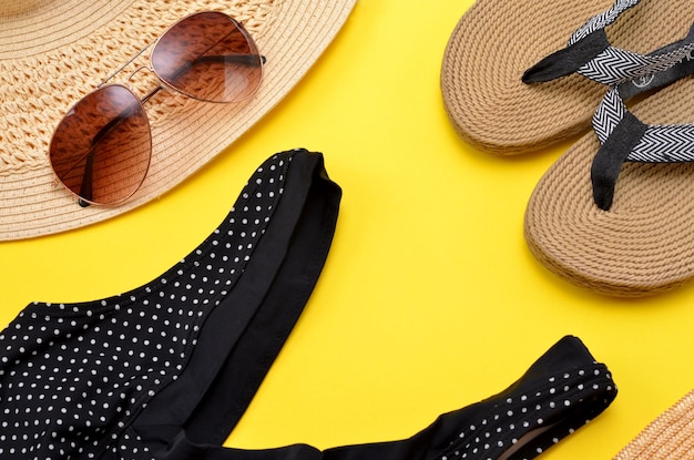 Items for summer holidays swimwear hat sunglasses and flip flops on a yellow background