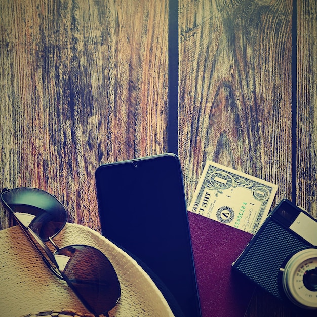 Предметы для летних каникул камера паспортсмартфон деньги шляпа солнцезащитные очки деревянный фон вид сверху с копией пространства красивая летняя концепция для путешествий и летних каникул
