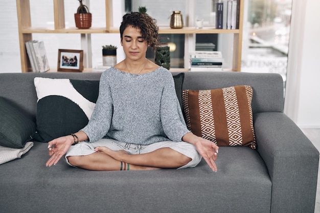 Its about mastering yourself Shot of an attractive young woman meditating on a sofa at home