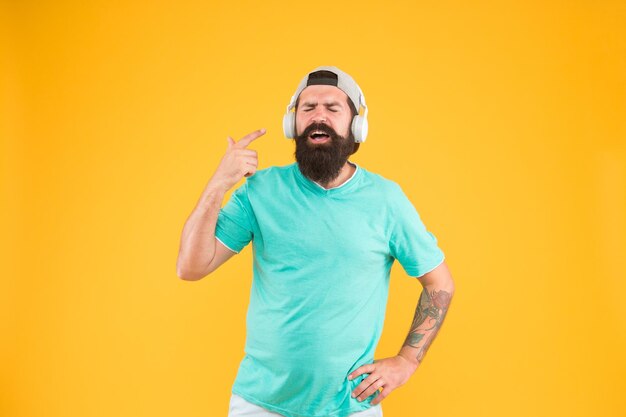 Its all about music Hipster enjoying his favorite music on yellow background Brutal guy listening to music and singing along to a song Bearded man wearing headphones playing music