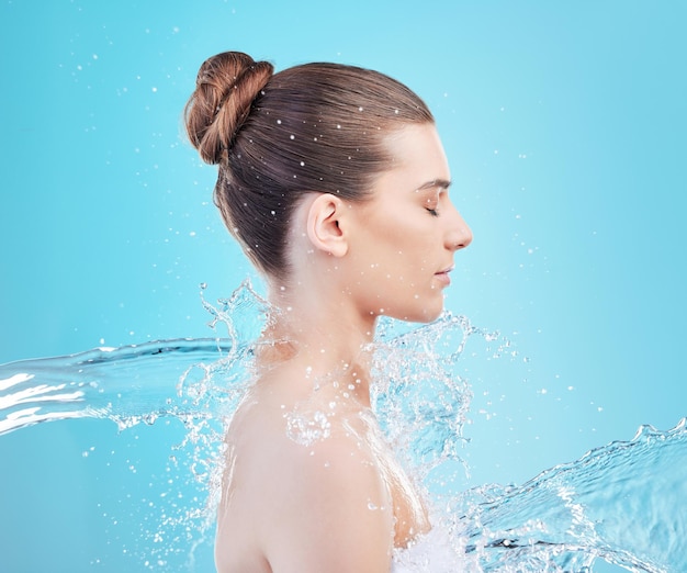 Its amazing what a shower does. Shot of a beautiful young woman being splashed with water against a blue background.