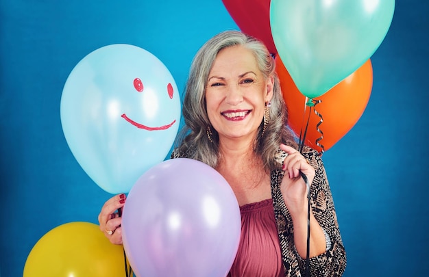 Its my birthday today portrait of a cheerful senior woman posing holding balloons in studio against a blue background