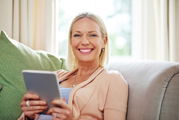 Its my connection to the world Portrait of a mature woman using her tablet while sitting on the sofa at home