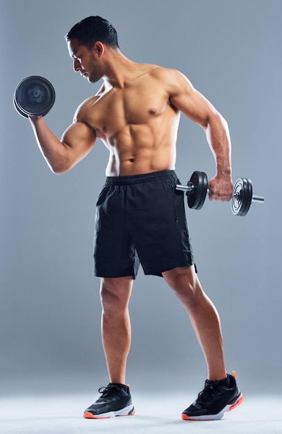 Its my goal to keep making muscles Studio shot of a muscular young man exercising with dumbbells against a grey background