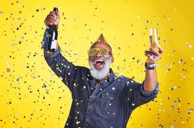 黄色の背景にスタジオでシャンパンを祝って飲んでいる陽気な年配の男性の肖像画を祝う時間