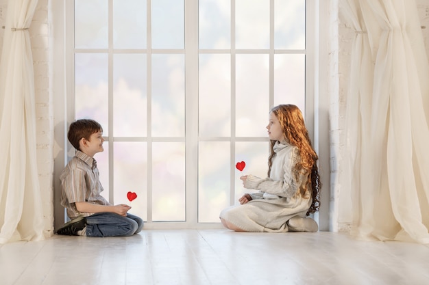 Ittle children sitting near window with red lollypops 