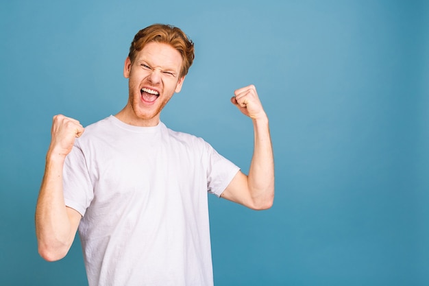 Ja! gelukkige winnaar! gelukkige jonge knappe man die de overwinning viert, gebaren maakt en de mond openhoudt