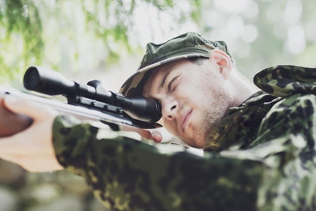 jacht, oorlog, leger en mensen concept - jonge soldaat, ranger of jager met geweer gericht en schietend in het bos