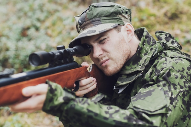 jacht, oorlog, leger en mensen concept - jonge soldaat, ranger of jager met geweer gericht en schietend in het bos