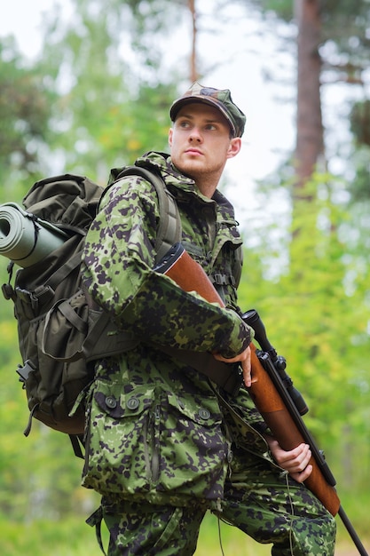 jacht, oorlog, leger en mensen concept - jonge soldaat, ranger of jager met pistool in bos