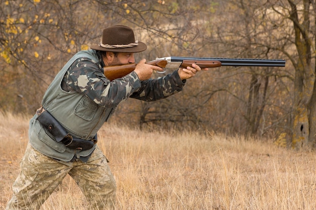 Jachtperiode, herfstseizoen geopend. Een jager met een pistool in zijn handen in jachtkleding in het herfstbos op zoek naar een trofee. Een man staat met wapens en jachthonden het wild op te sporen.