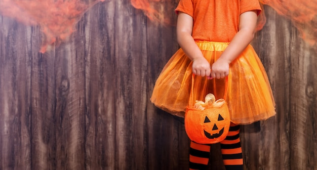 Jack o lantern a basket for sweets in the hands of a child girl in a witch costume on a wooden background