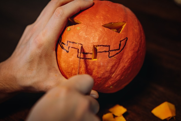 Photo jack's halloween pumpkin. man's hands carving mouth with paper knife. image with selective focus . high quality photo