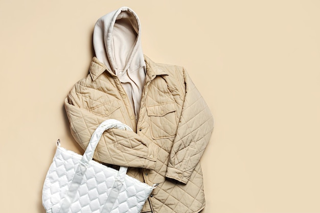 Jacket,  white hoody with quilted bag  on beige background. Fashion sweatshirt, casual youth style, sports. Stylish autumn or spring  clothes.