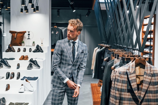 В пиджаке с галстуком Молодой парень в современном магазине с новой одеждой Элегантная дорогая мужская одежда
