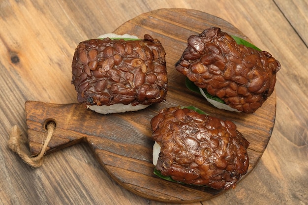 jadah ketan tempe bacem. savory sticky rice, tempeh bacem on a wooden cutting board. banana leaf.