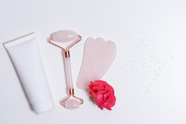 Jade massager roller and face cream on a white isolated background with a rose Place for your design