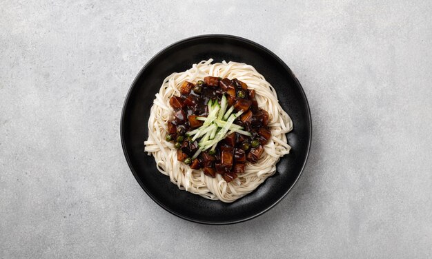 Корейская лапша Jajangmyeon в соусе из черной фасоли на светлом бетонном фоне, вид сверху