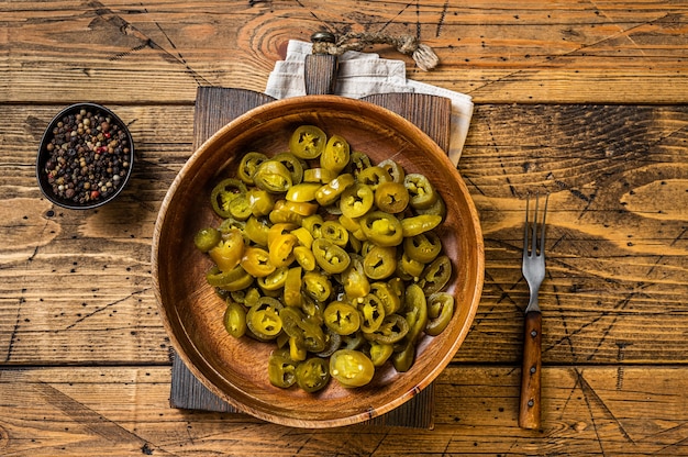 Jalapenos pickled and sliced, in old wooden plate . Wooden background. Top view.