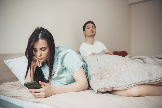 Jaloerse blanke man probeert te kijken naar wie zijn vriendin aan het typen is, met behulp van een telefoon in bed