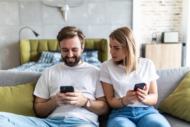 Jaloerse vrouw vriendje bespioneren en kijken naar zijn mobiele telefoon zittend op de bank thuis