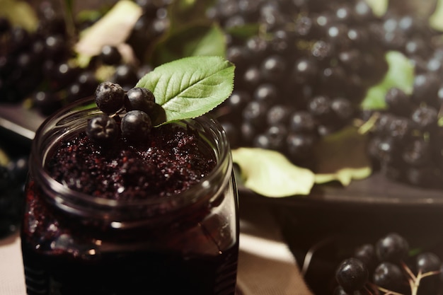 Jam from black chokeberries ( Aronia melanocarpa ) and its berries on dark table. Homemade preserves.