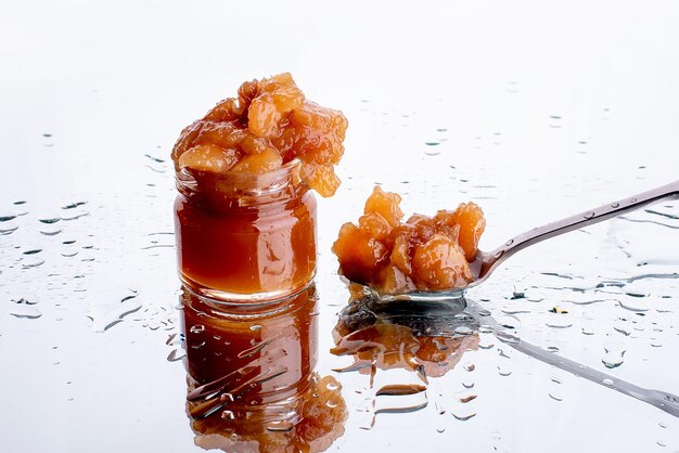 Jam in een pot en een lepel appel- en perenjam in een lepel op een witte spiegelachtergrond met waterdruppels, gezond natuurlijk dessert conceptxA