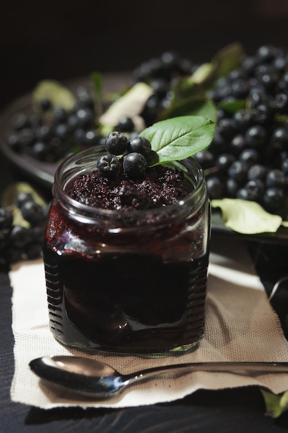 Jam van zwarte appelbessen (Aronia-melanocarpa) en zijn bessen op donkere tafel. Zelfgemaakte jam.