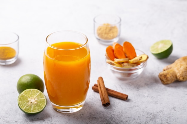 Bevanda jamu da radici di zenzero curcuma e lime in vetro su sfondo bianco