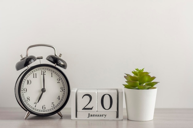 木製のカレンダーの1月20日、レトロな目覚まし時計とライトテーブルのミニポットの多肉植物の隣。1月のある日。冬の日。スペースのコピー。職場。