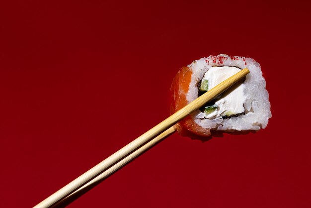 Foto le bacchette giapponesi tengono un rotolo di salmone su uno sfondo bordeaux