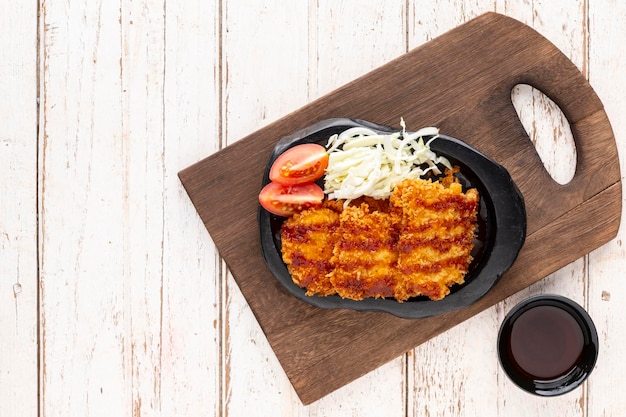 Cotoletta di maiale fritta giapponese o tonkatsu con salsa di cavolo e pomodoro in piatto di ceramica nera su vecchio tagliere di legno su fondo di legno bianco con copia spazio per la vista del tavolo superiore del testo