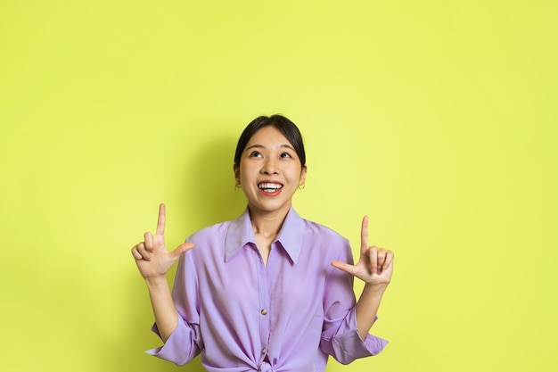 Japanese Female Pointing Fingers Up Standing Over Yellow Studio Background