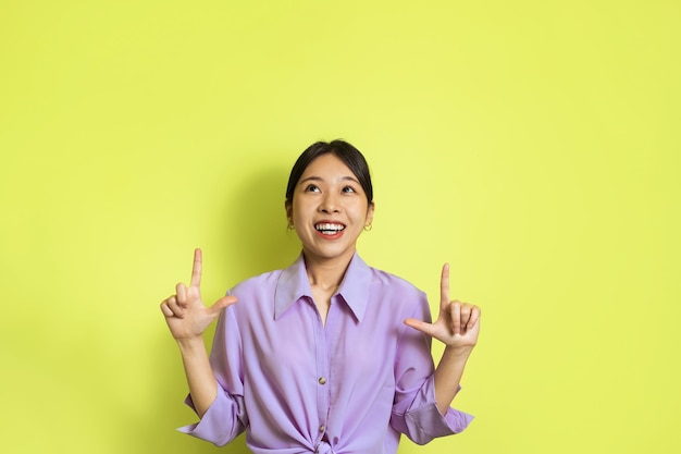 Japanese female pointing fingers up standing over yellow studio background