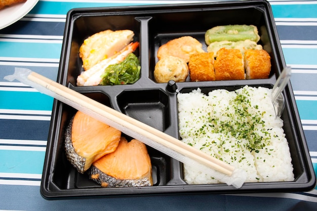 Japanese food bento box rice and fried salmon and vegetables with other cuisine on table in garden at outdoor of Japan village in Ayutthaya Thailand