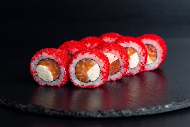 Photo japanese food, portion of sushi in red masago caviar isolated on black background.