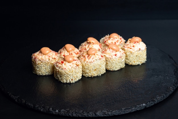 Японская еда, острые роллы в белых семенах кунжута с острым соусом на черном фоне.