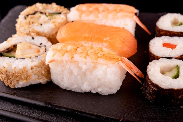 japanese food with sushi rolls with salmon tuna shrimp with black chopsticks on black background