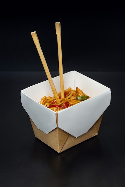 Cibo giapponese, noodles wok udon con carne e verdure in una scatola aperta isolata su uno sfondo solido.
