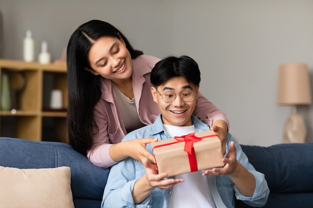 Japanese girlfriend giving wrapped present box to surprised boyfriend indoor