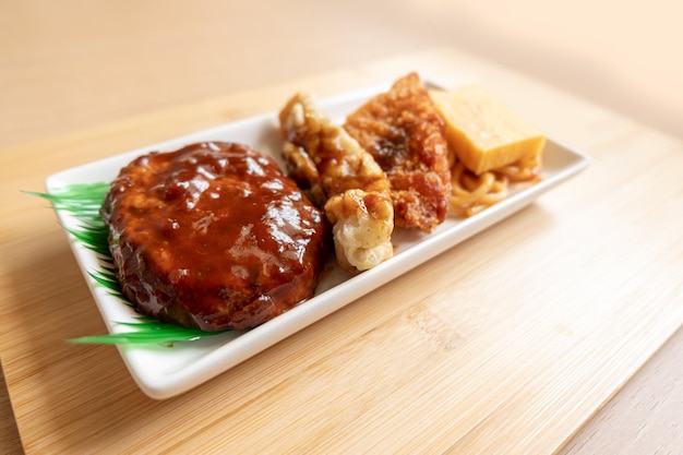 Japanese hamburger steak fried fish and Japanese rolled omelet on white plate