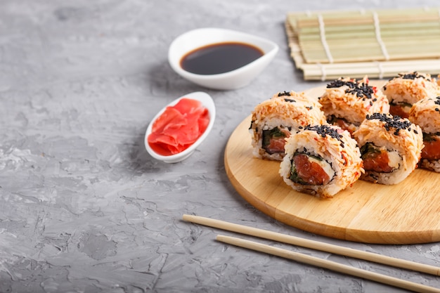 Japanese maki sushi rolls with salmon, sesame, on wooden board on gray concrete 