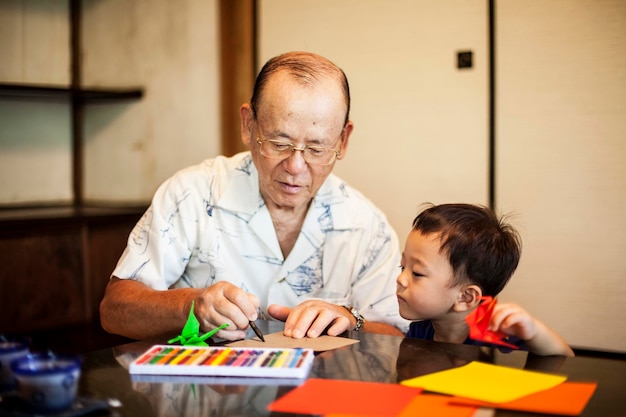 日本人男性と小さな男の子がテーブルに座って、鮮やかな色の折り紙を使って動物を作る