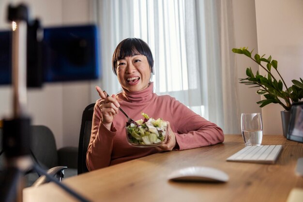 Foto una donna giapponese di mezza età che mangia un pasto sano e fa una videoconferenza a casa