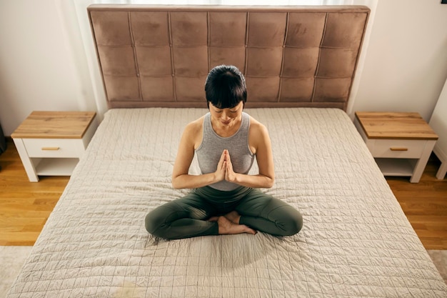 Японка средних лет медитирует в спальне.