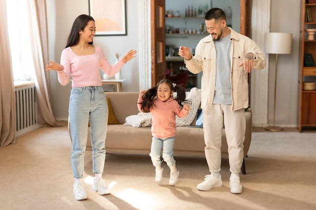 Japanese parents and baby daughter playing and laughing dancing indoors