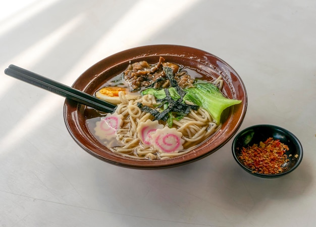 白いテーブルの上のボウルに箸と海藻卵麺のスープが入った日本のラーメンスープ