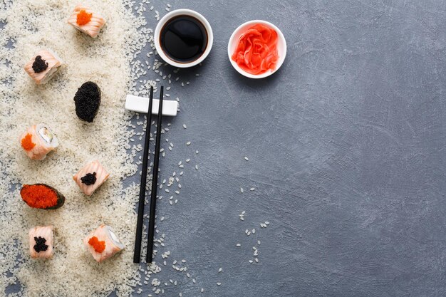 Japanese restaurant, sushi roll and gunkan platter. Set for one person with black chopsticks, ginger, soy on rustic grey and rice background. Top view, copy space